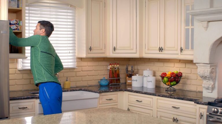 Man reaching into a kitchen cabinet in a warmly lit, modern home kitchen
