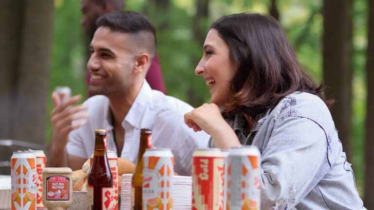 Friends enjoying drinks and laughter at a picnic table with Stiegl beer cans in the foreground