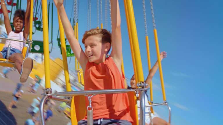 Kids enjoying a colorful swing ride at an amusement park under a clear blue sky